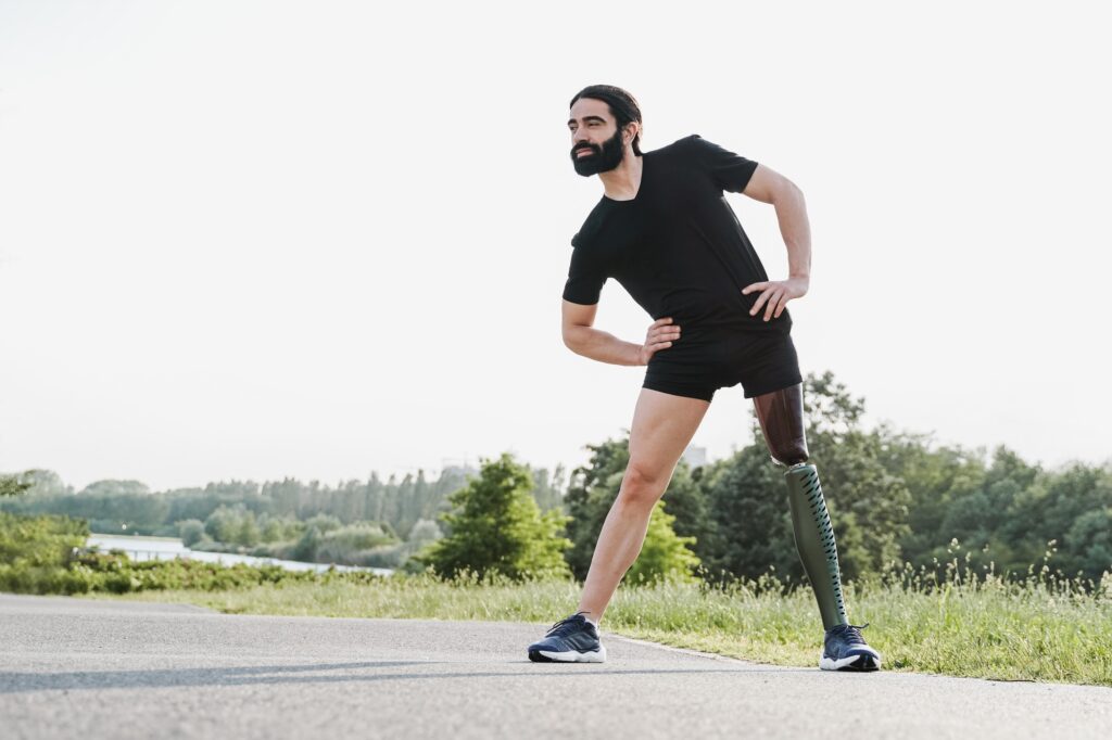 Fit man with physical disability stretching before exercise outdoor - Focus on prosthetic leg
