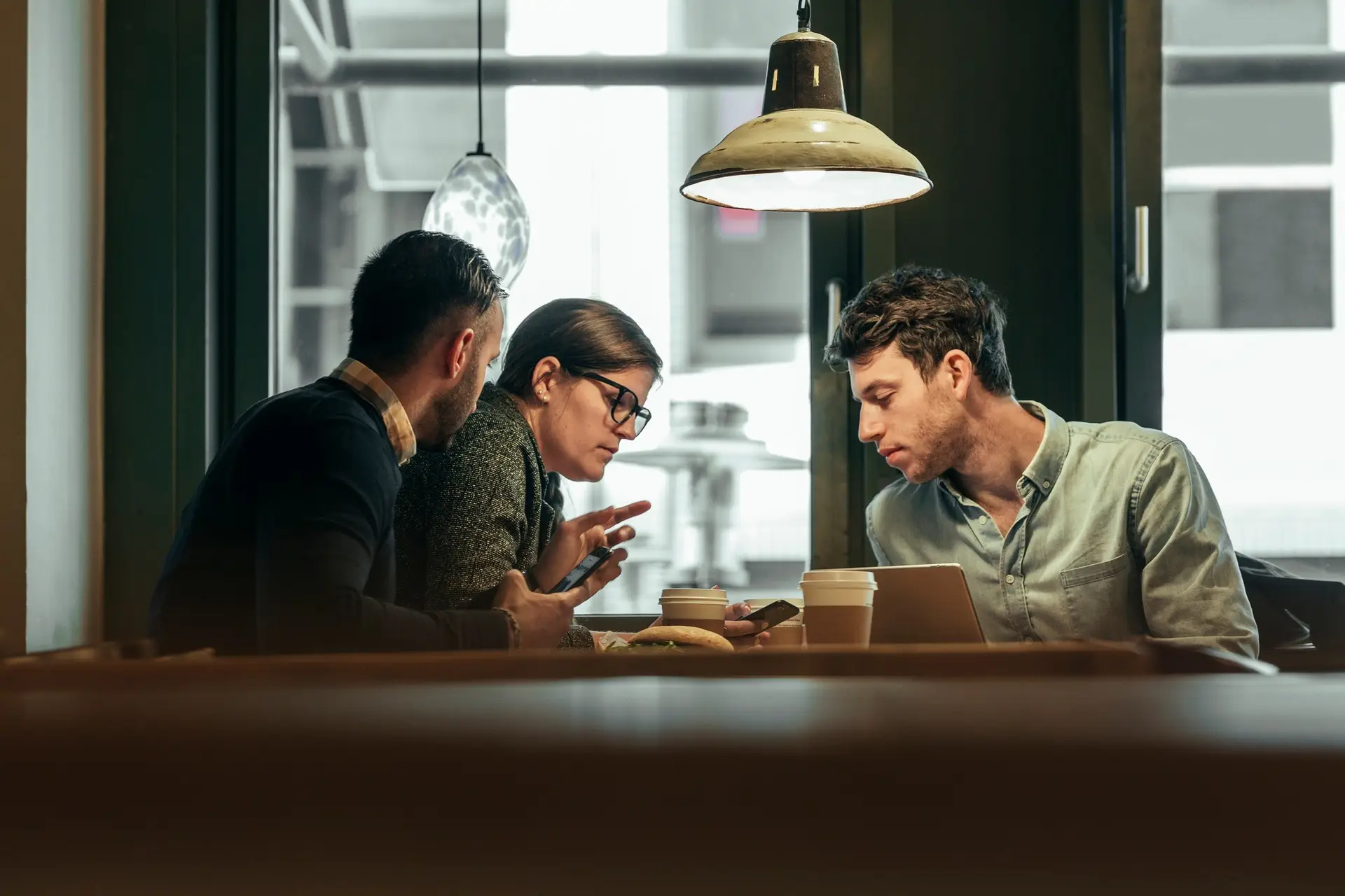 Group of three people sitting in cafeteria and looking at smart phone