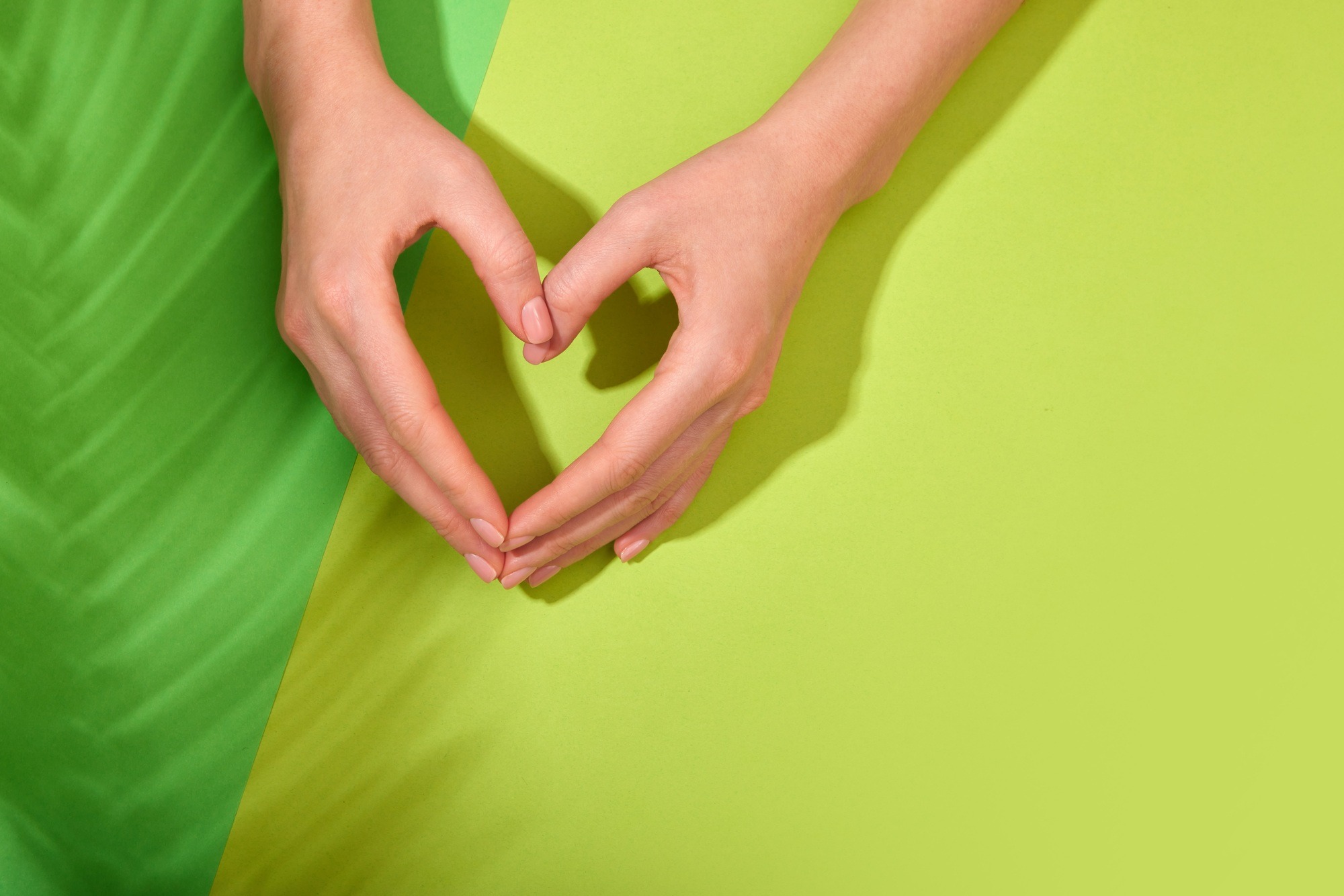 Hands making heart symbol on green background